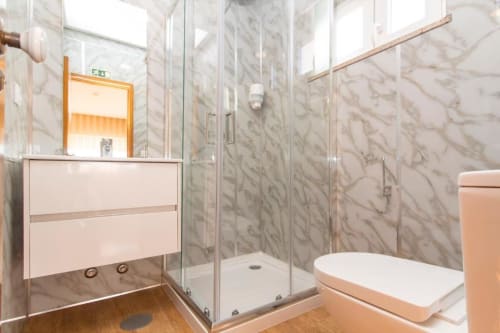 Banheiro moderno com mármol no Sleep & Go hostel, com box de vidro, armário branco e piso de madeira