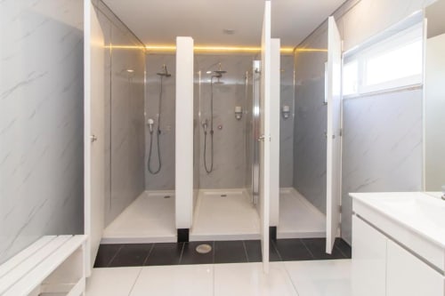 Casa de banho compartilhada moderna no hostel Sleep & Go em Esposende com múltiplos chuveiros, paredes em mármore e equipamentos contemporâneos