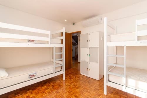 Dormitório misto limpo com beliches brancos, piso de madeira e armazenamento no Sleep & Go hostel em Esposende, Portugal