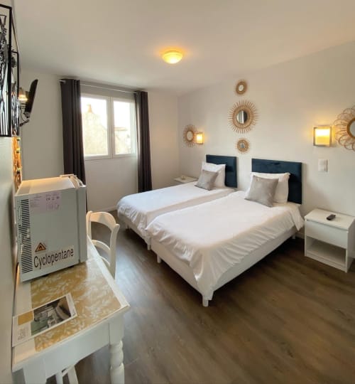 Chambre twin de l'Hôtel le Vauban à Carentan : deux lits blancs, têtes de lit noires et décoration murale soleil doré