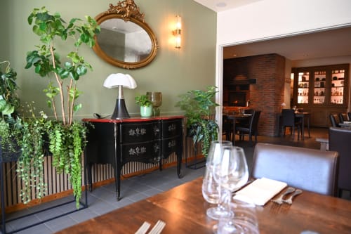 Élégante salle à manger du Au Bon Gîte aux murs sage, plantes en pot et accès au bar en brique