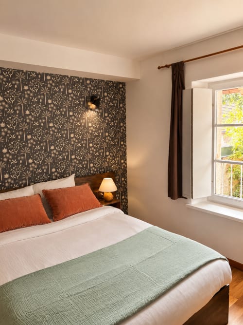 Chambre double cosy à Au Bon Gîte avec tête de lit fleurie, literie blanche, jeté vert, oreillers orange et vue jardin