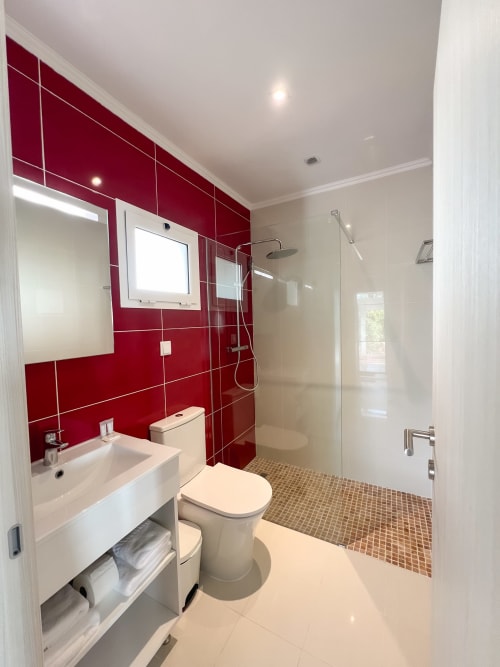 Banheiro moderno com azulejos vermelhos, pia branca, vaso sanitário e chuveiro walk-in no hotel Monte Horeb, Nadadouro Portugal
