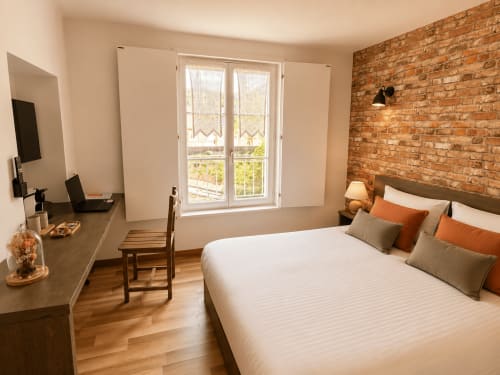 Chambre double à Au Bon Gîte avec lit blanc, mur en briques apparentes, bureau et fenêtres avec vue sur le jardin