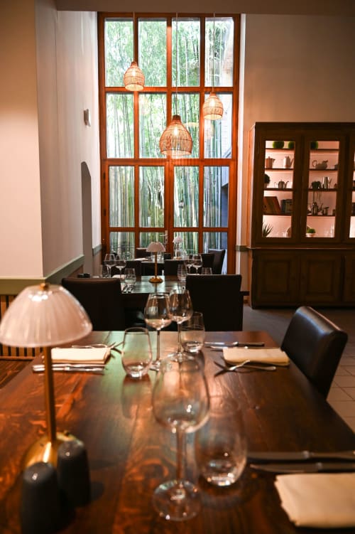 Élégante salle à manger du Au Bon Gîte avec table en bois, verres à vin et vue sur le jardin de bambous par de grandes baies vitrées