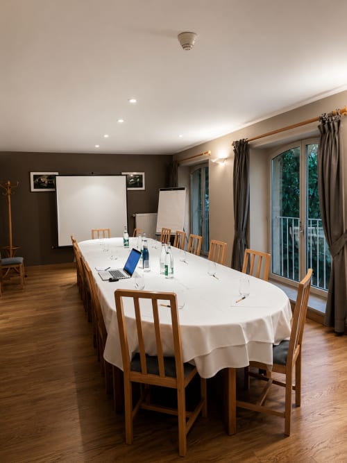 Salle de réunion Au Bon Gîte avec table ovale, chaises en bois, écran de projection et vue sur le jardin à Senones
