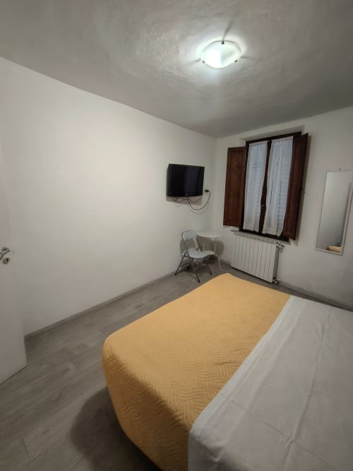 Bedroom in Casa di Alfredo apartment, Siena. Bed with yellow blanket, wall-mounted TV, chair, and heating radiator under