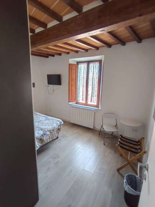 Spacious apartment bedroom at Casa di Alfredo in Siena with wooden beamed ceiling, flat-screen TV, and window with landmark
