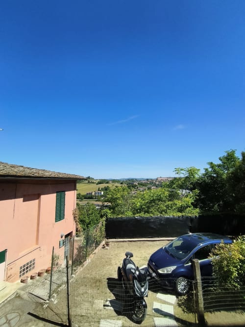 Peach-colored apartment with countryside view near Siena, Italy. Parking area with scooter and car visible.