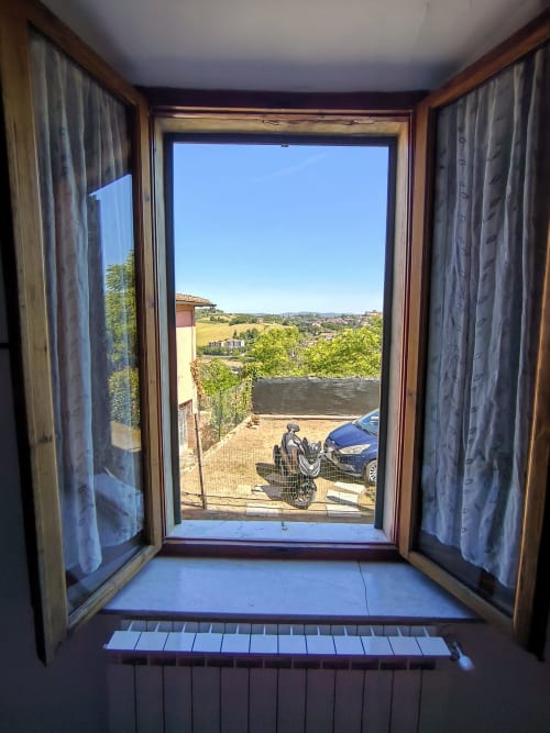 Open French doors at Casa di Alfredo in Siena overlook countryside landscape with parked motorcycle and distant hills