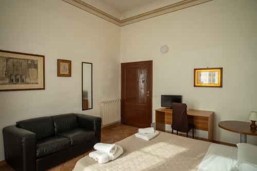 Camera spaziosa di Casa di Alfredo B&B a Siena con letto, divano nero, scrivania, TV e accesso alla vista del giardino