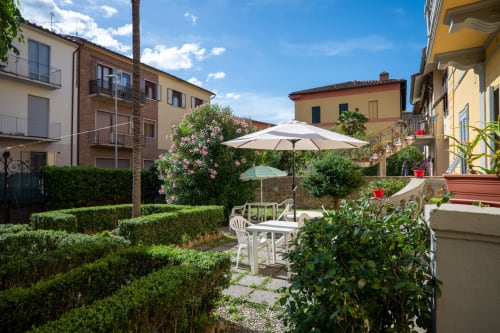 Patio del giardino toscano di Casa di Alfredo B&B a Siena con ombrelloni bianchi, sedute, piante fiorite e edifici storici.