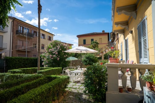 Cortile soleggiato di Casa di Alfredo a Siena con ombrelloni bianchi, vasi in terracotta, siepi e edifici storici