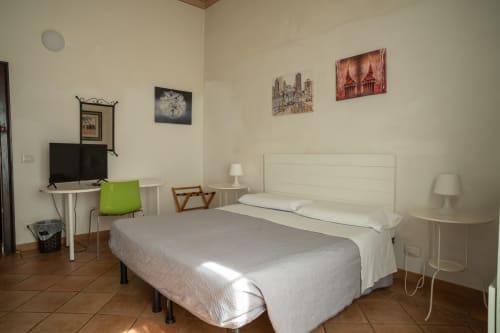 Camera luminosa a Casa di Alfredo a Siena con letto matrimoniale, testata bianca, poltrona verde, scrivania con TV e vista giardino