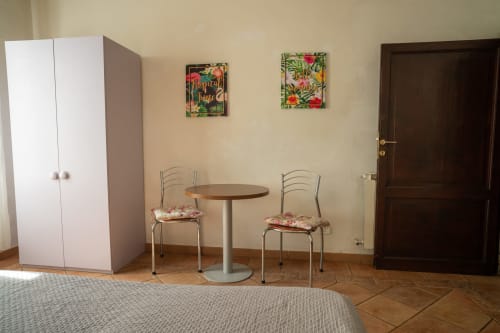 Stanza luminosa a Casa di Alfredo a Siena con tavolo rotondo, due sedie, guardaroba e arte con veduta giardino