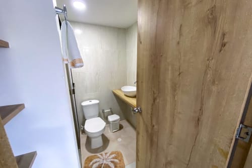 Baño moderno en apartamento Olamar Living con inodoro, lavamanos, tocador de madera y ducha en hotel Santiago de Tolú