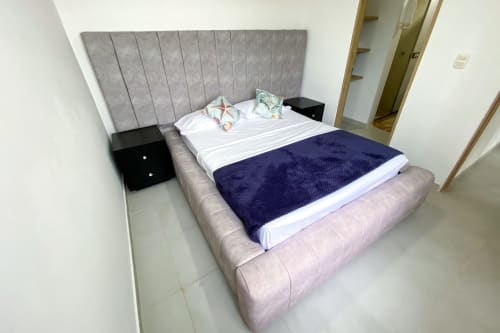 Dormitorio moderno del hotel Olamar Living en Santiago de Tolú con cama tapizada gris, ropa de cama azul marino y mesitas negras