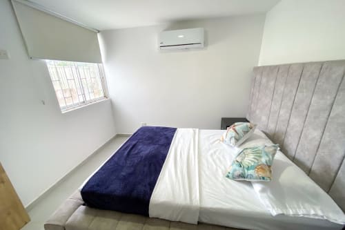 Habitación moderna del hotel Olamar Living en Santiago de Tolú con aire acondicionado, cabecero tapizado gris y vista a la ventana