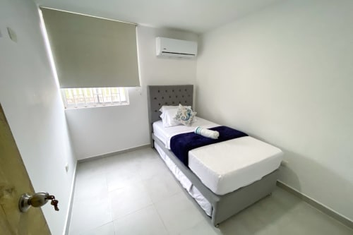 Habitación moderna en Olamar Living de Coveñas con cama individual, cabecero gris, aire acondicionado y ventana con persiana enrollable