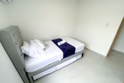 Cama impecablemente hecha con sábanas blancas y manta azul marino en apartamento Olamar Living, Coveñas, Colombia