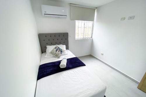 Dormitorio moderno en Olamar Living en Santiago de Tolú con cabecero capitoné gris, ropa blanca, aire acondicionado y luz natural