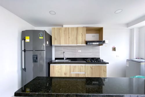 Cocina moderna en apartamento Olamar Living con encimera de granito oscuro, muebles de madera, estufa a gas y salpicadero negro