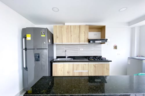 Cocina moderna con encimera de granito oscuro, armarios de madera clara, estufa a gas y refrigerador de acero inoxidable en Olamar