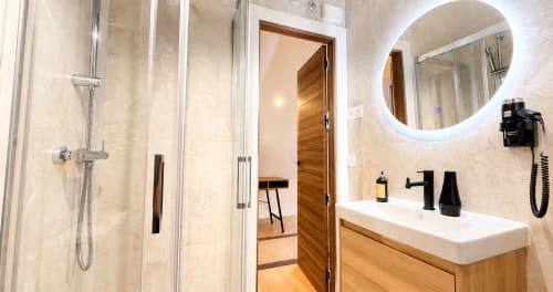 Baño moderno en La Posada de las Flores con ducha, espejo redondo, puerta de madera y lavabo blanco
