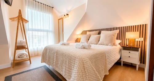 Luminoso dormitorio doble moderno en La Posada de las Flores con cabecero de madera, ropa de cama color crema y luz natural desde la ventana