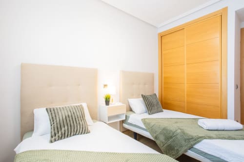 Twin bedroom at Haus Holiday Homes, Los Alcázares with beige headboards, striped pillows, and wooden wardrobe