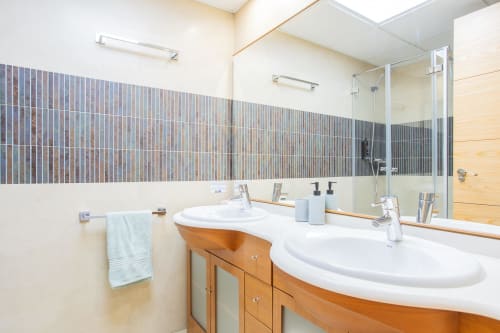 Modern bathroom with dual white sinks, wooden vanity, striped tile backsplash, and walk-in shower at Haus Holiday Homes