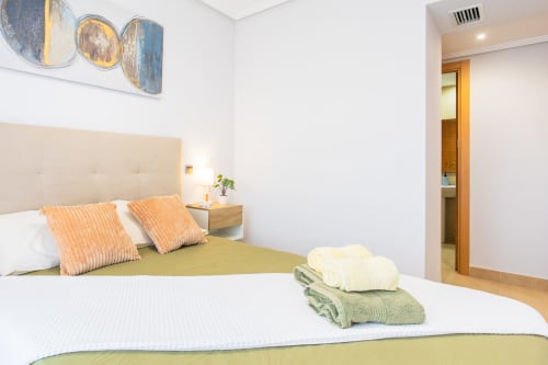 Modern bedroom at Haus Holiday Homes in Los Alcázares with white linens, orange pillows, and sea view balcony access