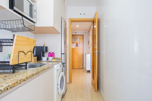 Modern kitchen with granite countertop, white cabinetry, wooden door leading to hallway in Los Alcázares apartment