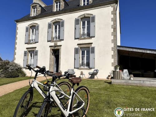 Deux vélos garés sur la pelouse devant La Belle Epoque, une charmante maison en pierre blanche aux volets à Kerlaz, France