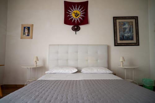 Camera da letto con testiera rivestita in bianco, copriletto grigio e quadri incorniciati presso Casa di Alfredo B&B a Siena, Italia