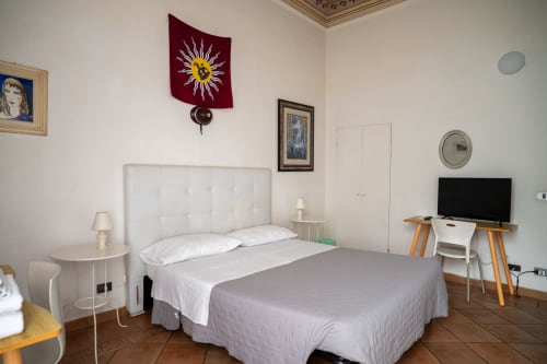 Camera luminosa della Casa di Alfredo B&B a Siena con letto bianco, scrivania e orologio rosso a muro