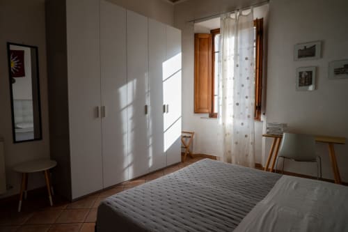 Camera luminosa di Casa di Alfredo a Siena con armadi bianchi, mobili in legno e vista sul giardino dalle finestre con persiane