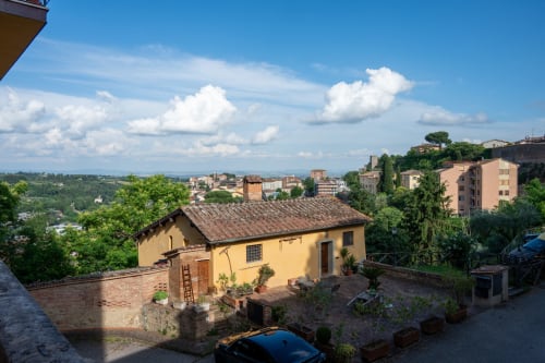 Casa di Alfredo, guesthouse a Siena con edifici in terracotta gialla, vista sul giardino e paesaggio toscano ondulato
