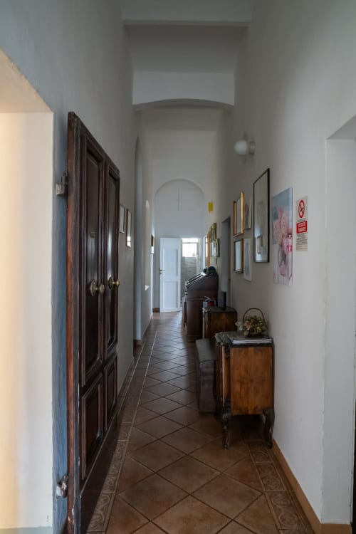 Lungo corridoio della Casa di Alfredo a Siena con porte in legno scuro, opere d'arte incorniciate e pavimento in terracotta