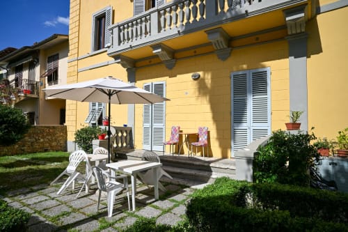 Terrazza Casa di Alfardo B&B Siena con villa gialla, ombrellone bianco, sedie e vista sulla campagna