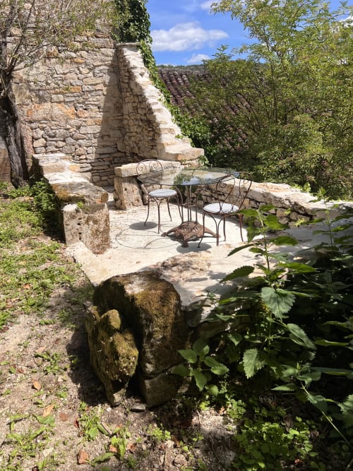 Terrasse en pierre avec mobilier en fer forgé donnant sur le jardin de Cénevières à la Maison d'hôtes Noubar