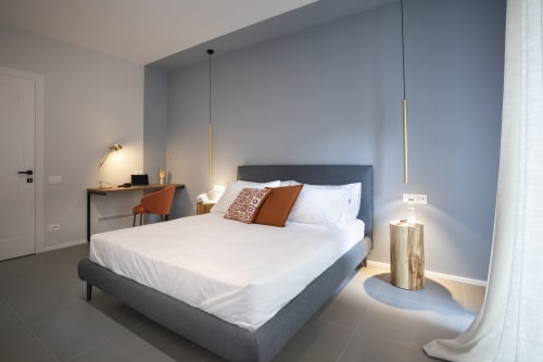 Modern bedroom at Camere d'Aria BnB in Locana with gray bed, white linens, orange accents, desk, and pendant lighting