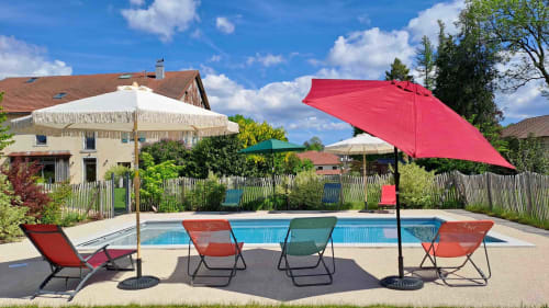 Espace piscine de La Pause ô Logis avec parasols rouges, transats et maison à Saint Laurent en Grandvaux