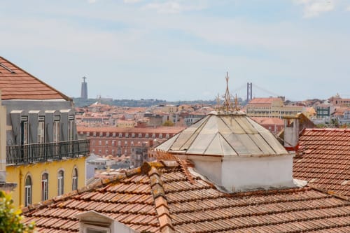 Lisbon Poets Inn rooftop view with terracotta tiles, white dome structure, and cityscape with Tagus bridge