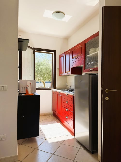 Cucina compatta e luminosa con pensili rossi, elettrodomestici in acciaio inox e vista sul giardino alla villa A Mare Case Vacanze