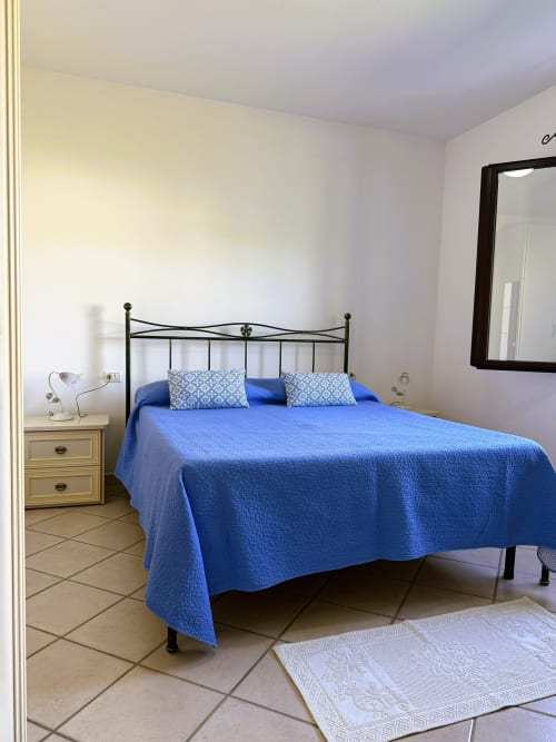 Camera luminosa con copriletto trapuntato blu, letto in ferro battuto e comodino bianco presso la villa A Mare Case Vacanze