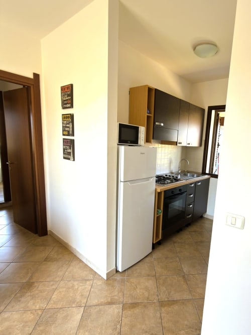 Cucina moderna nell'appartamento di Valledoria con frigorifero bianco, fornello a gas, microonde e arredamento in legno