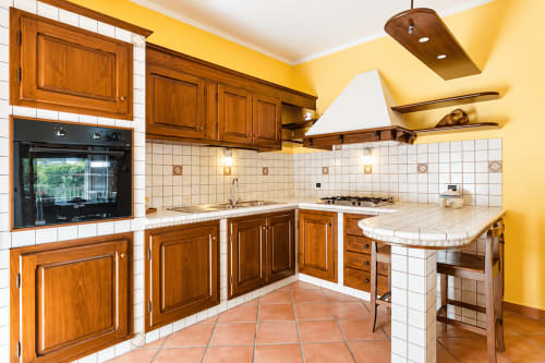 Cucina dal caldo giallo con mobili in legno, rivestimento in piastrelle bianche e pavimenti in cotto alla villa Trabocchi Livings di Borgo