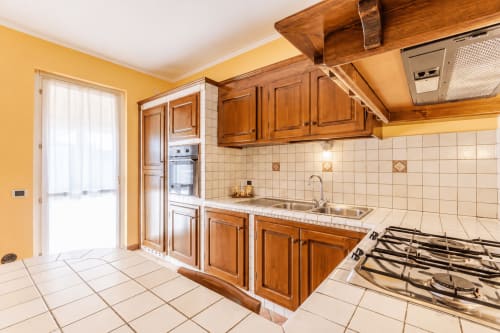 Cucina luminosa con toni giallo brillante, mobili in legno, fornello a gas e rivestimento piastrellato presso la villa Trabocchi Livings Borgo Dragani