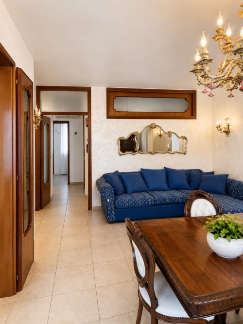 Elegante soggiorno in Appartamento Lisa con divano blu, mobili in legno, specchi decorati, lampadario e pavimento in ceramica